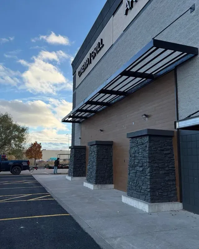 An exterior shot of a building with a gray brick facade, stone pillars, and a black metal awning under a cloudy sky.