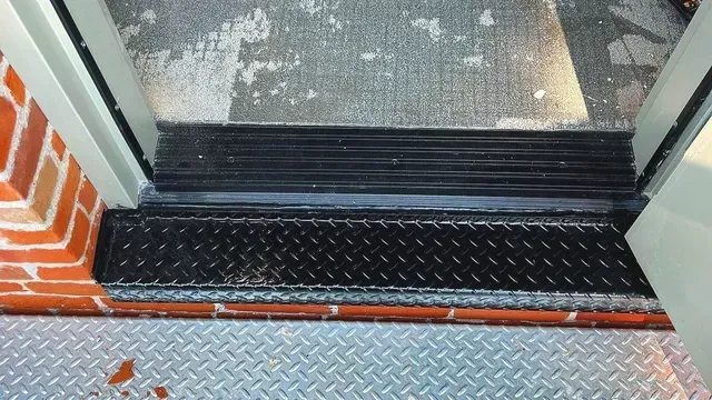 A doorway threshold featuring a black diamond-plate metal step and a ribbed rubber floor transition.