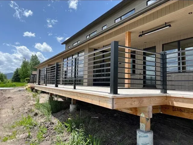 A modern home with a wooden deck featuring black horizontal metal railings, set against a sunny, blue sky.