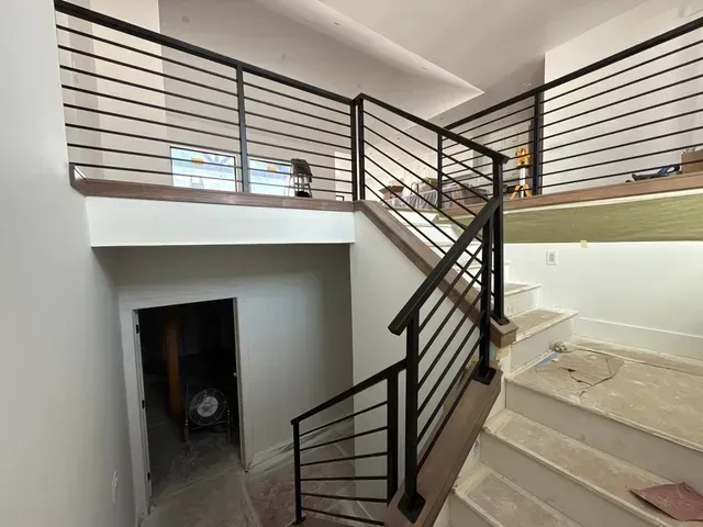 Modern staircase with dark metal horizontal railings leading up to a landing in a brightly lit residential interior.