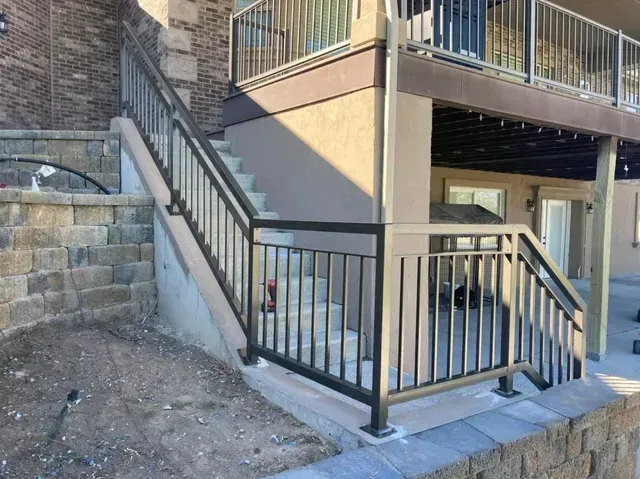 Metal railings surround concrete steps leading up to a deck attached to a building with stone siding.