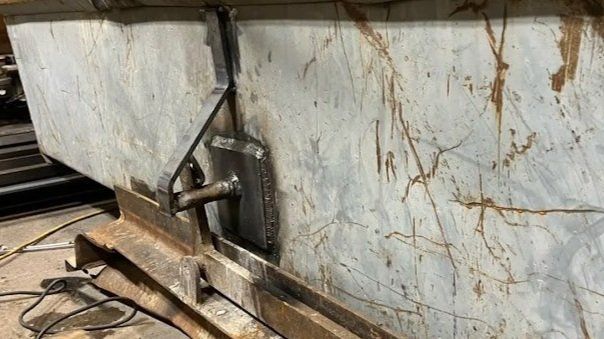 Welded metal hinge on a rusty metal container.