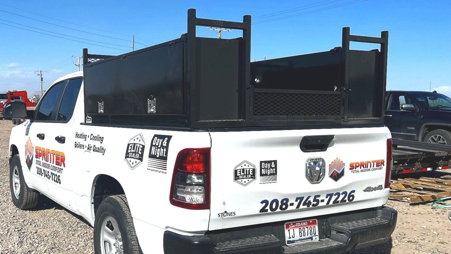 White work truck with black utility bed, multiple stickers, and a phone number on the tailgate.