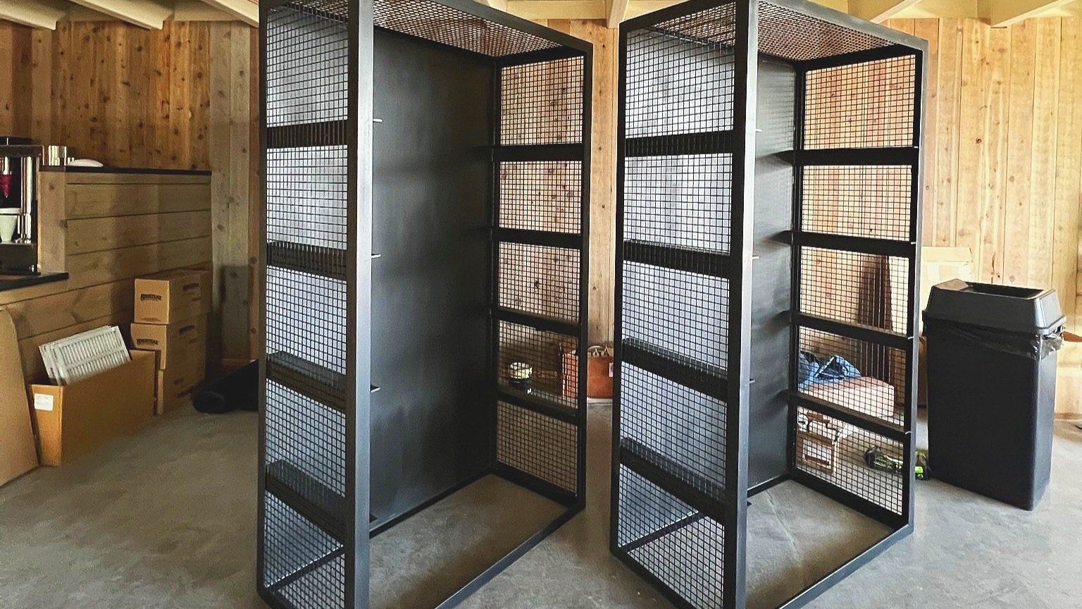 Two black metal storage racks with wire mesh sides and shelves in a wooden room.