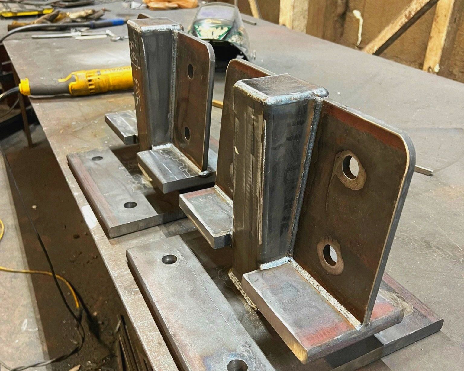Two welded steel brackets with bolt holes on a metal workbench.
