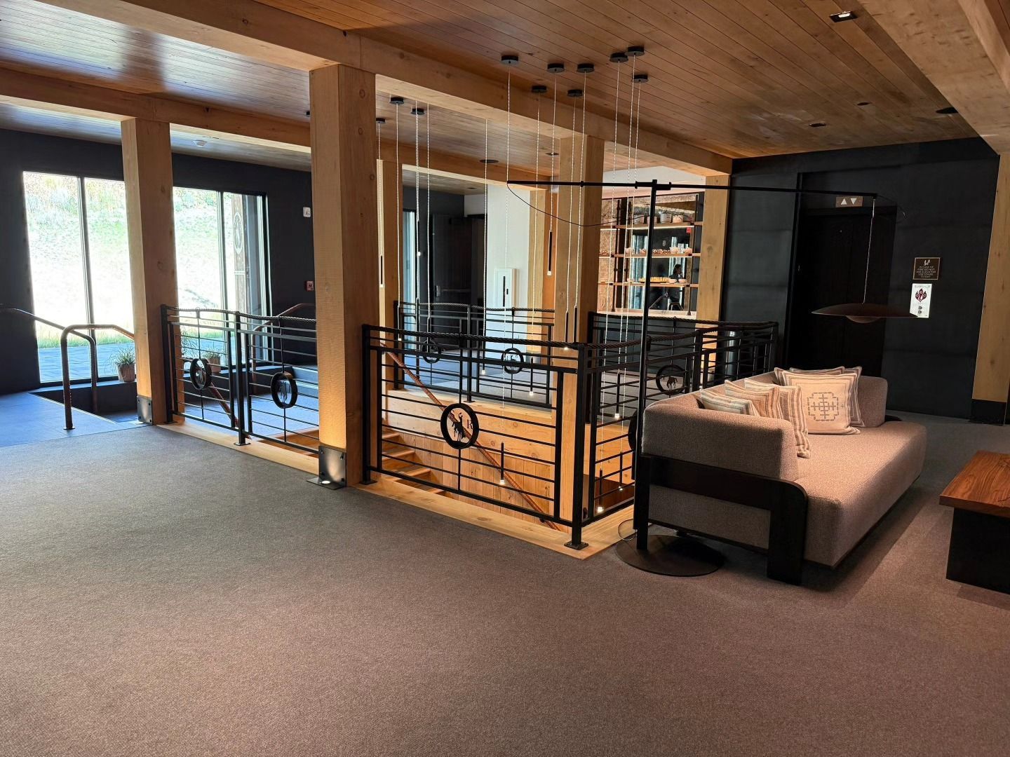 Lobby area with a sofa, railing, staircase, and windows. Brown columns and ceiling with gray carpet.