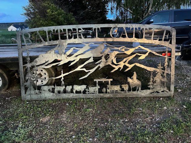 Metal sign depicting a mountain scene with cattle, a cowboy, and the words 