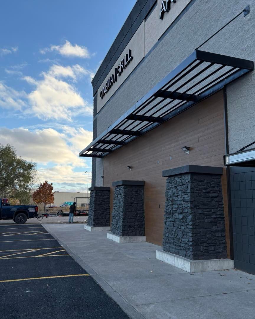 Exterior of a building with a black awning and pillars, overcast sky, parking lot in view.