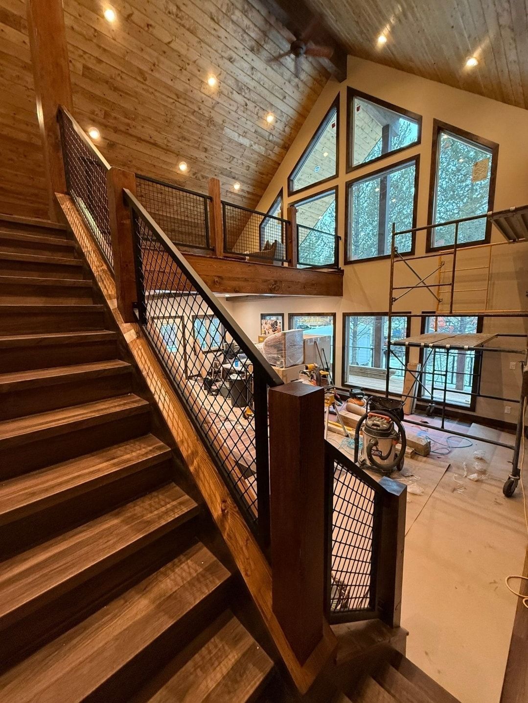 Wooden staircase with decorative iron railings leading up to a loft area with large windows.