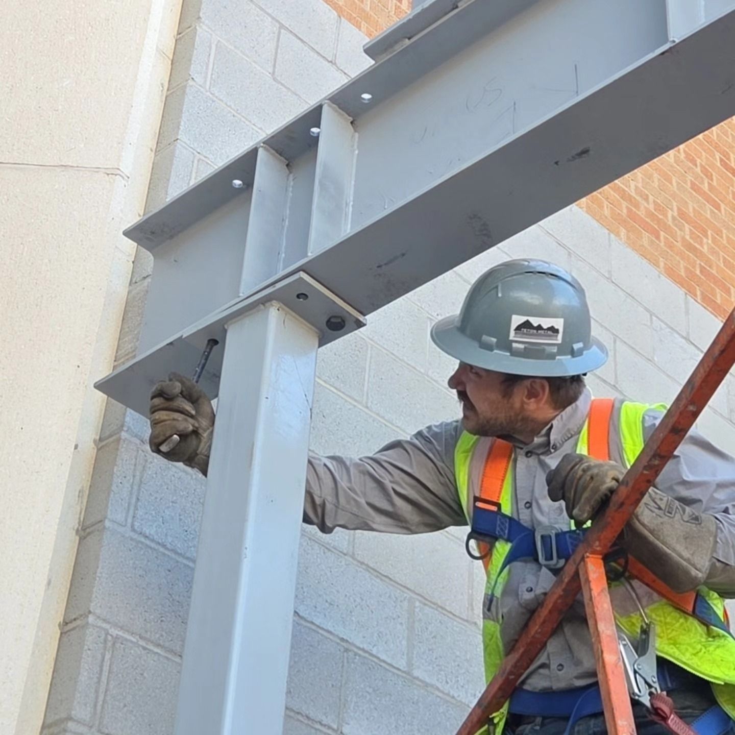 Construction worker in hard hat and safety vest, installing steel beam with bolts on a building.