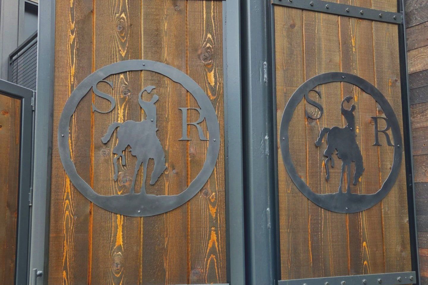 Wooden doors with metal circle logo featuring a bucking horse and 