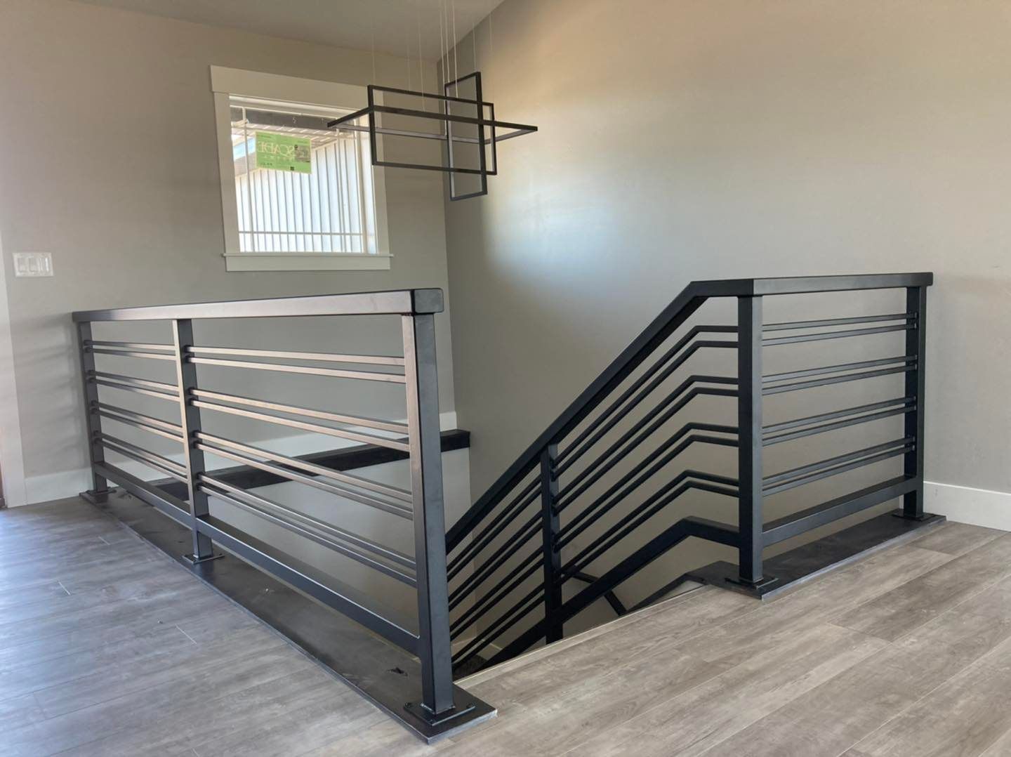 Staircase with black metal railing in a modern home. Gray walls, light wood flooring, and a window.