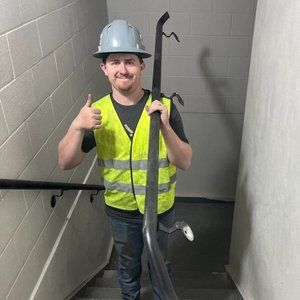 Man in safety gear holding a pipe, giving a thumbs-up on a staircase.
