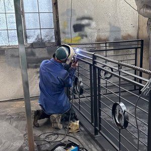 A person welding a metal railing in a workshop, wearing protective gear.