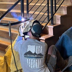 Welder in protective gear welding stair railing. Indoors, bright blue welding arc.
