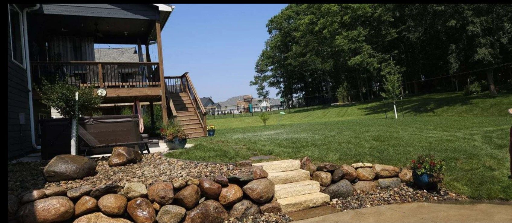 A house with a large lawn and a rock wall in front of it.