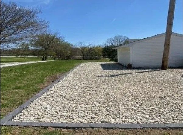 A gravel driveway leading to a garage with a house in the background.