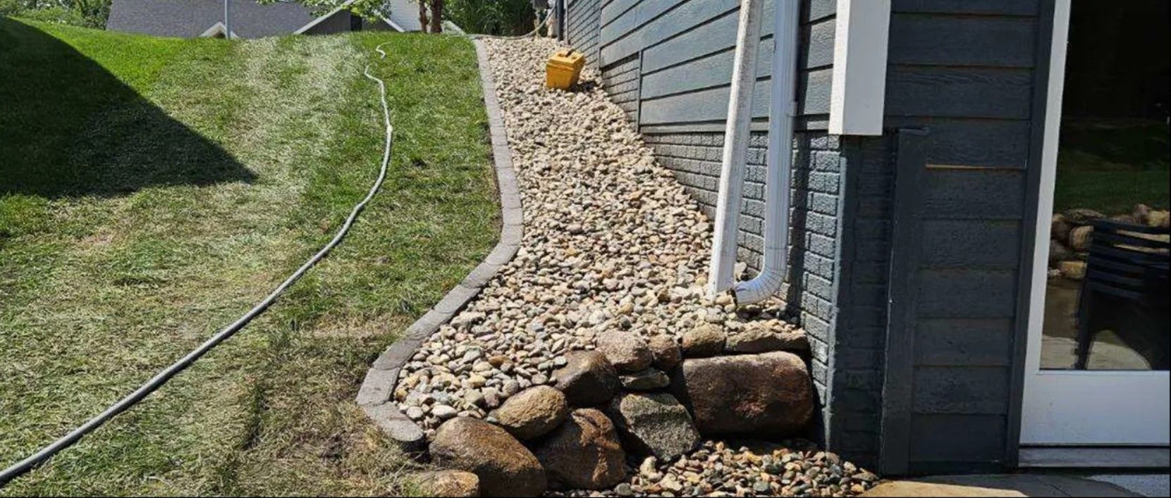 A sidewalk with rocks and a hose next to a house.