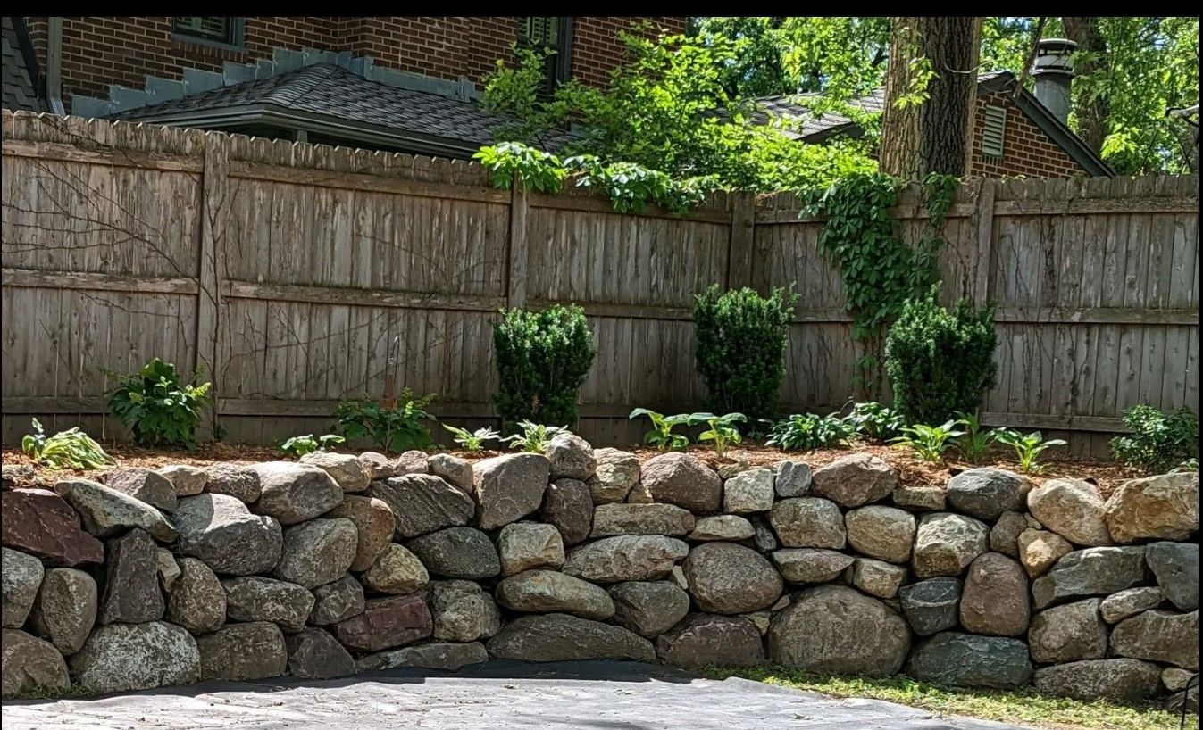 A stone wall with a wooden fence in the background