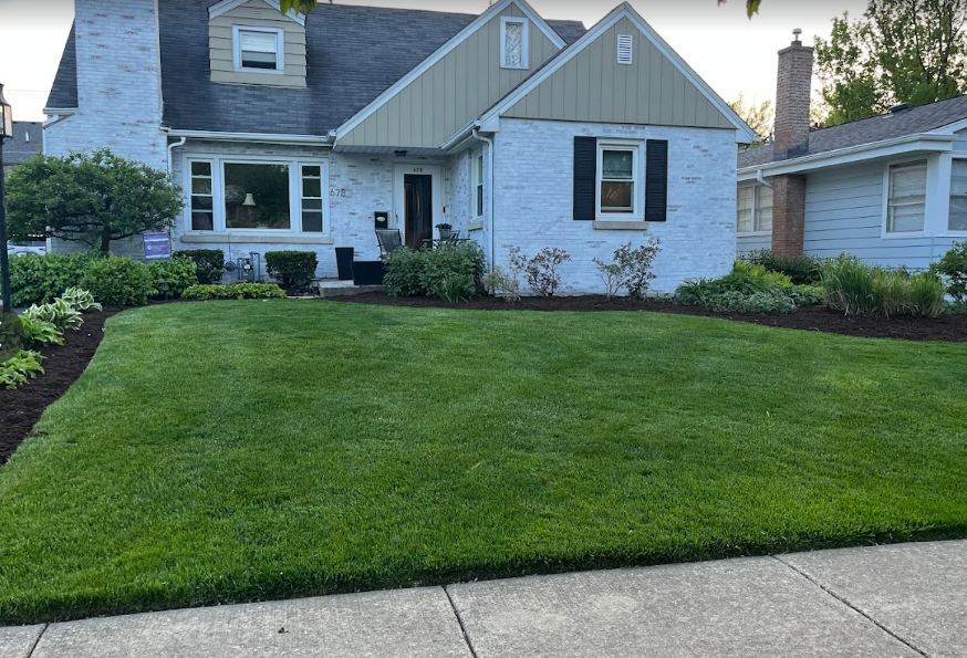 A white brick house with a lush green lawn in front of it.