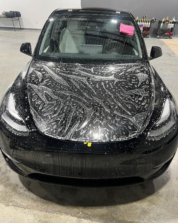 A black tesla model 3 is covered in plastic wrap.