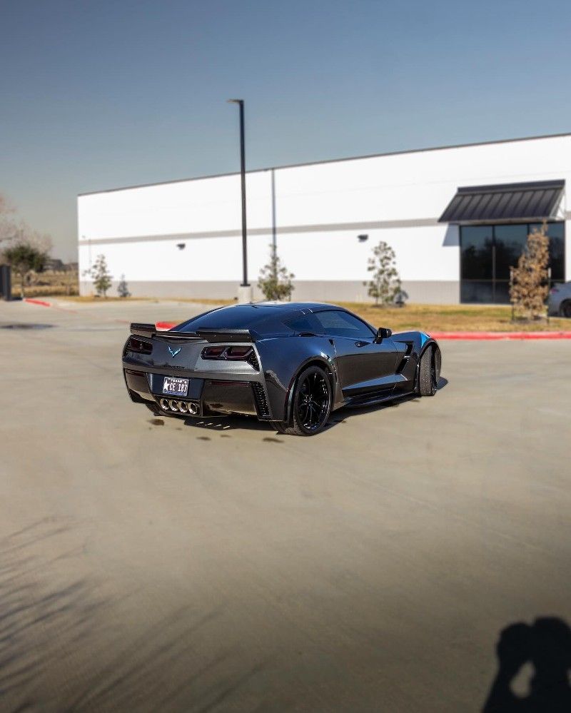 A black sports car is driving down a street in front of a building.