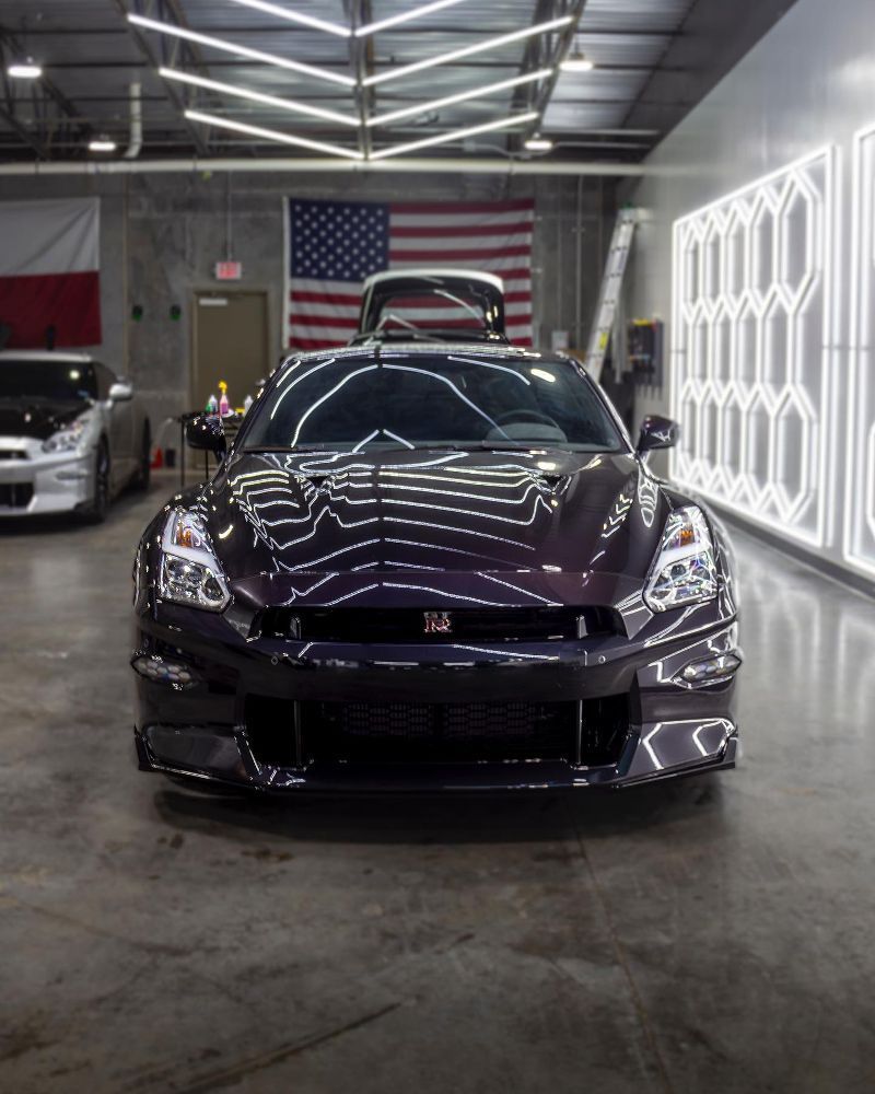 A purple sports car is parked in a garage with an american flag in the background.