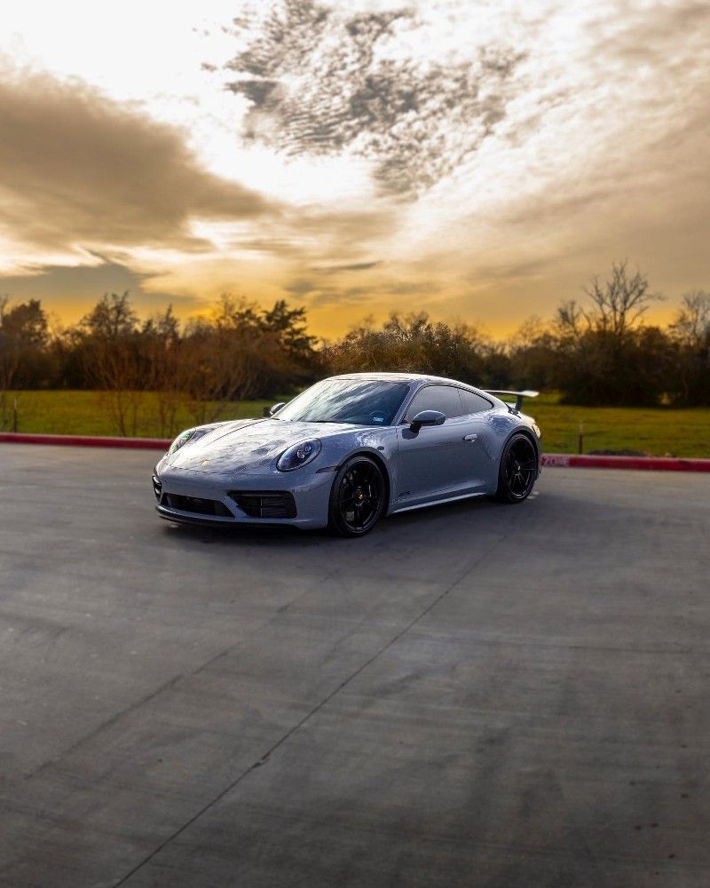 A silver sports car is parked in a parking lot at sunset.