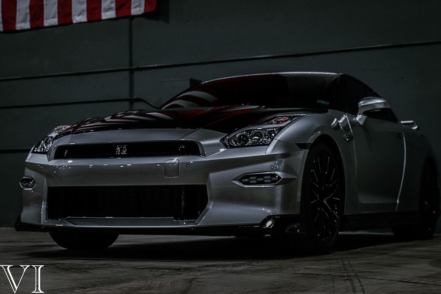 A silver sports car with an american flag on the hood is parked in a garage.