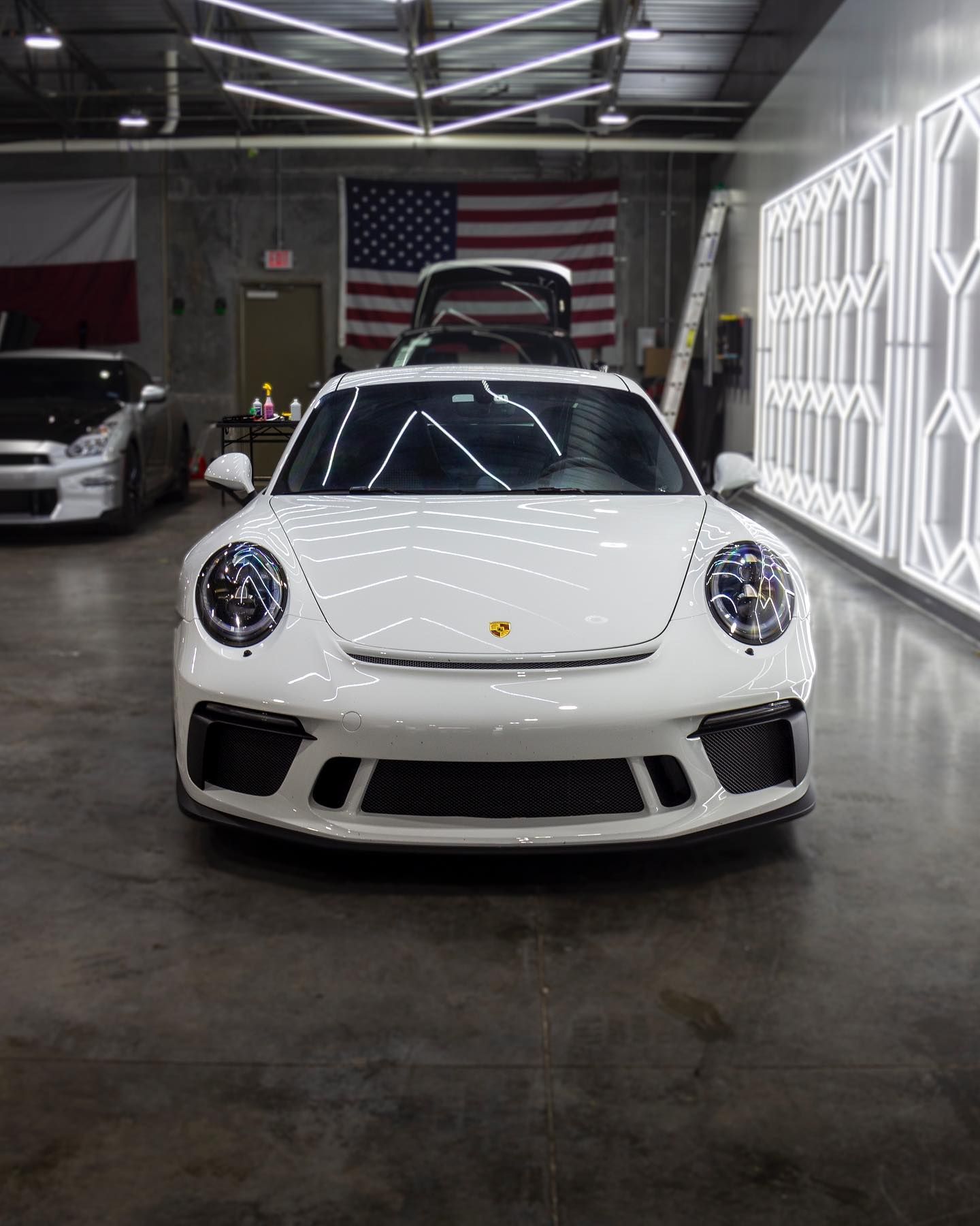 A white porsche is parked in a garage with the trunk open.