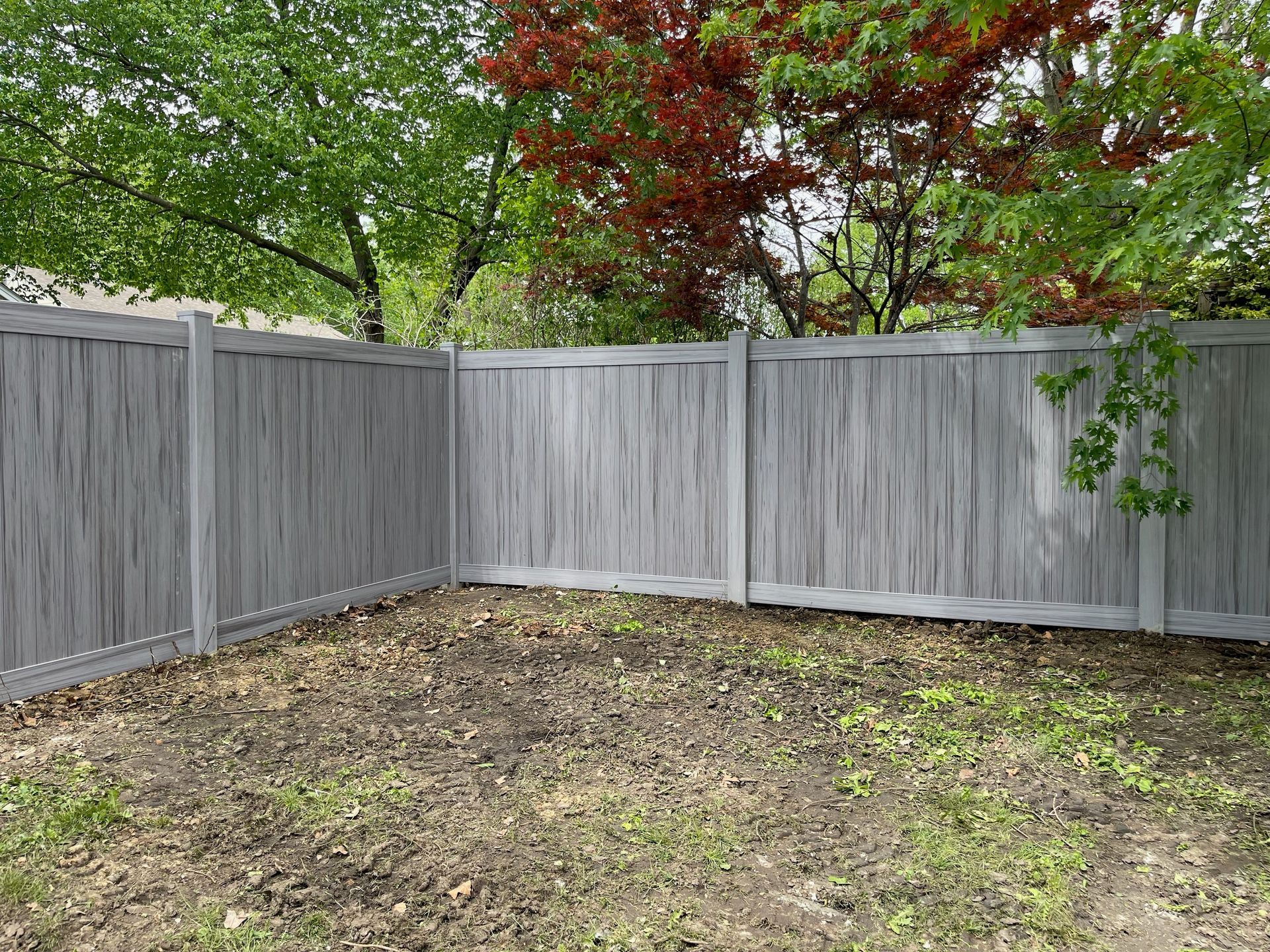 A gray wooden vinyl fence in a backyard with trees in the background