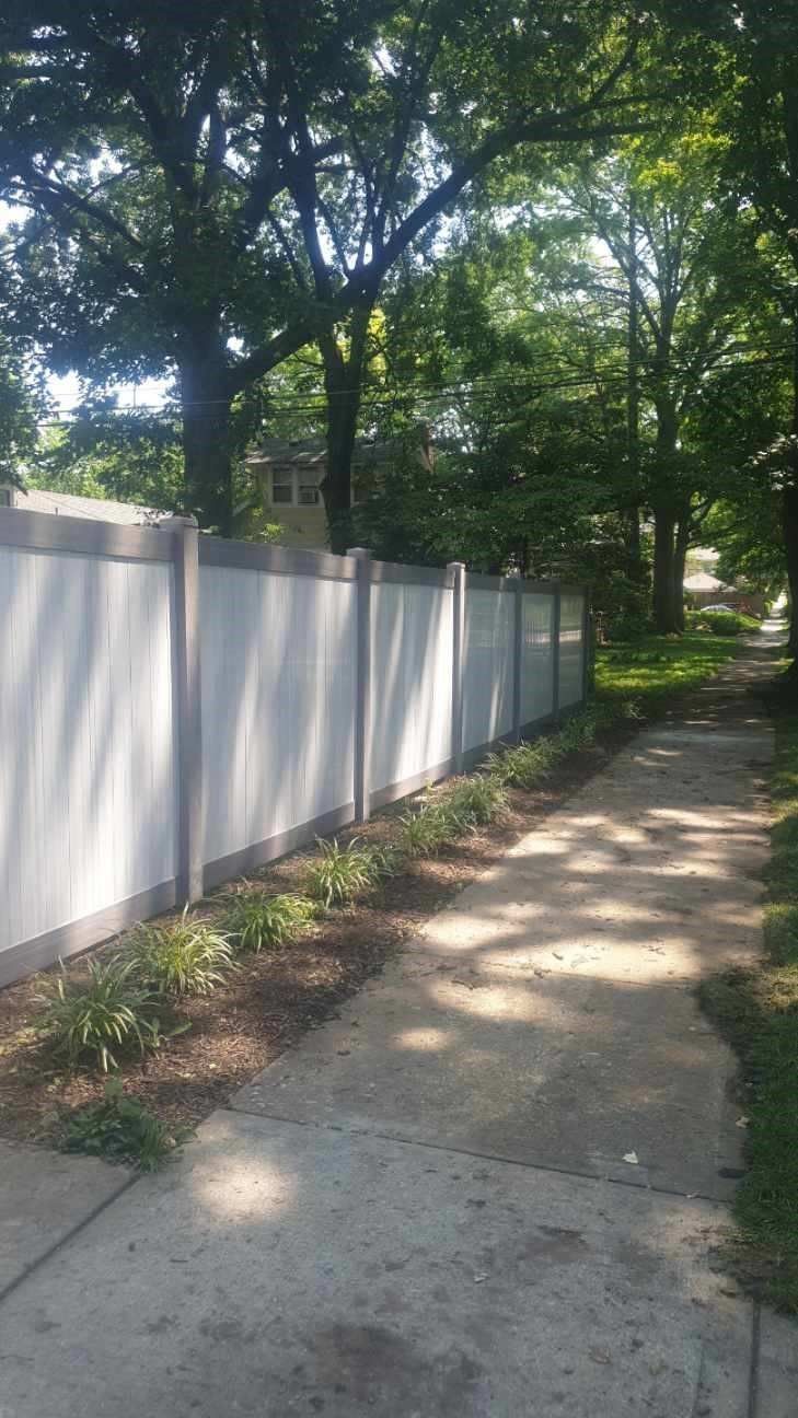 A gray vinyl fence along a sidewalk with trees in the background