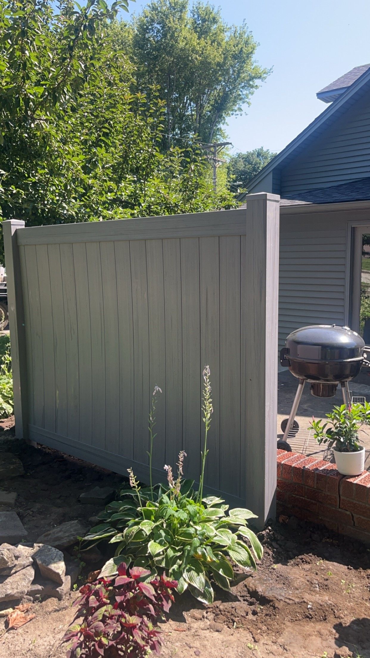 A gray vinyl fence in the middle of a garden next to a house