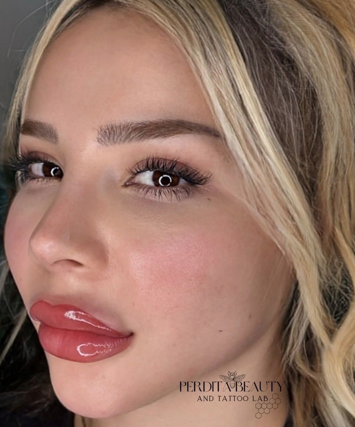 Woman with blonde hair and plump, glossy lips; has eyebrow and lip makeup.