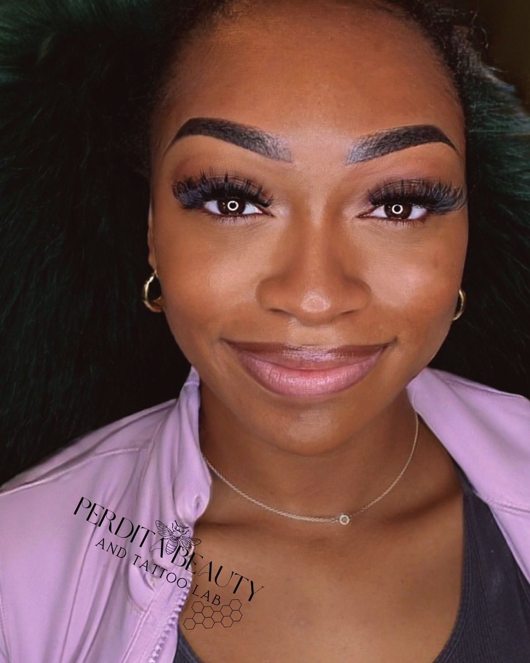 Woman with dark skin, long lashes, and a light pink jacket smiles, wearing a necklace.