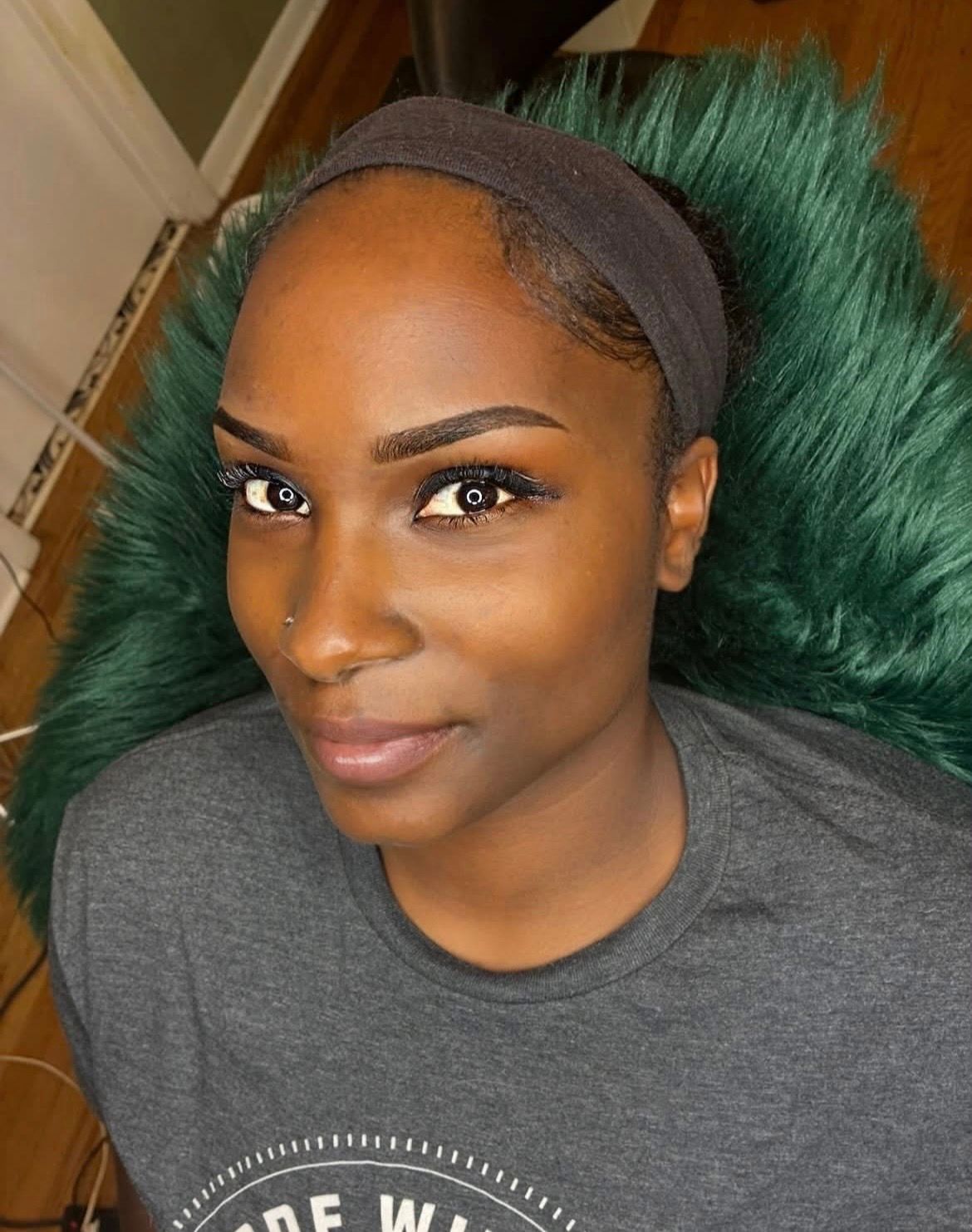 Close-up portrait of a person in a gray headband and T-shirt, reclining on a green furry chair.