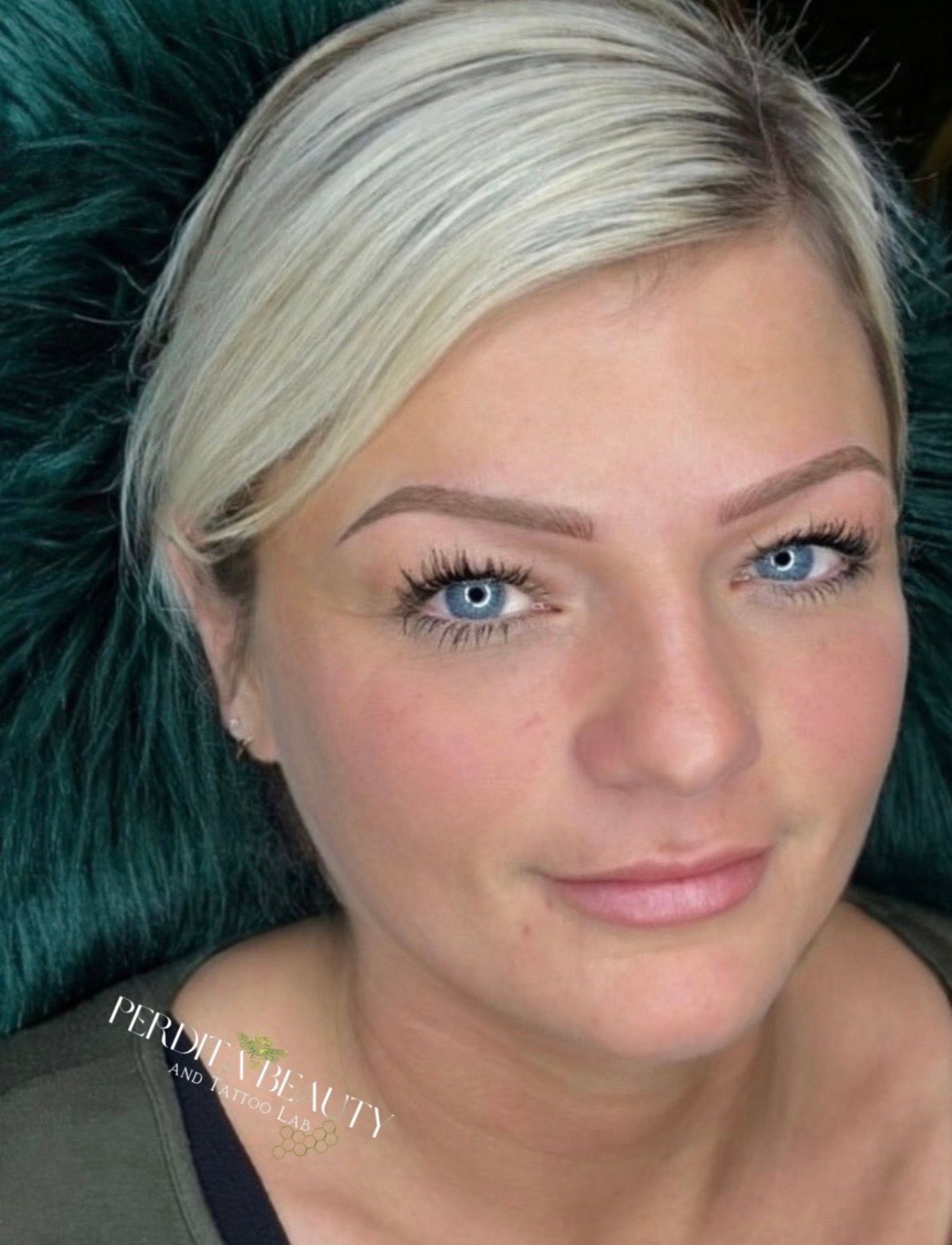 Close-up portrait of a woman with short blonde hair and blue eyes, looking at the camera on a dark teal background