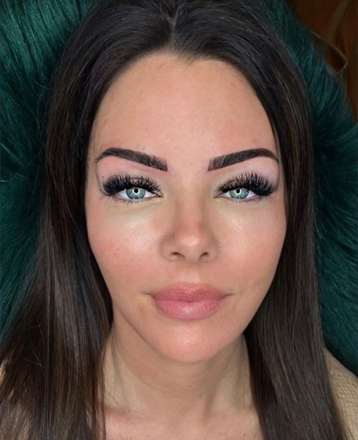 Close-up portrait of a woman with dark hair, blue eyes, and full makeup against a dark background