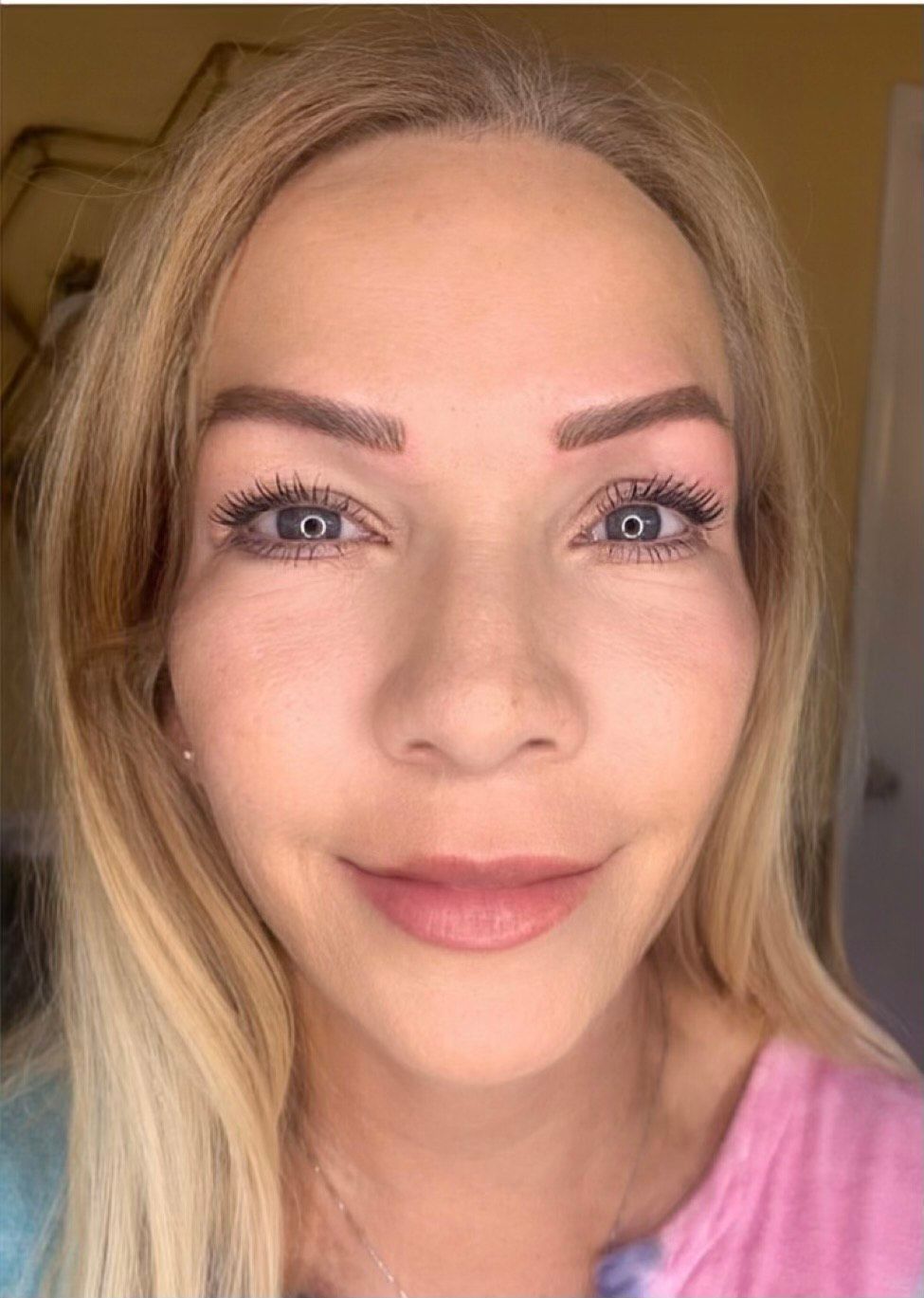 A close-up of a woman's face with blonde hair and a pink shirt.
