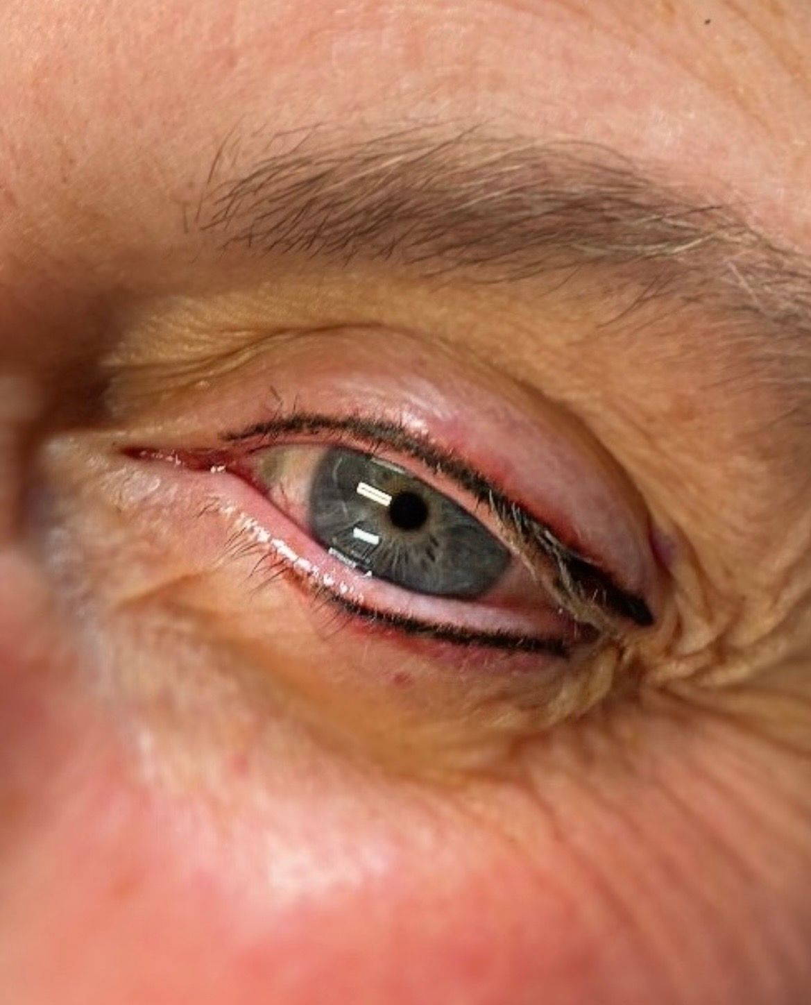 Close-up of a blue eye with black eyeliner. The eye is partially closed, showing wrinkles.