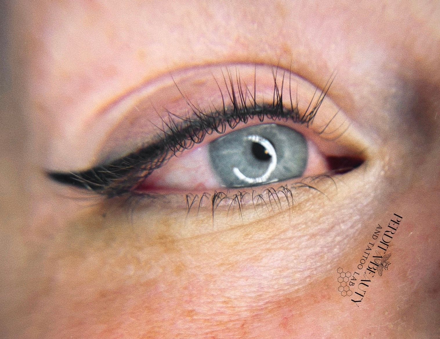 Close-up of an eye with permanent eyeliner. The eye is light blue with black eyeliner and eyelashes.