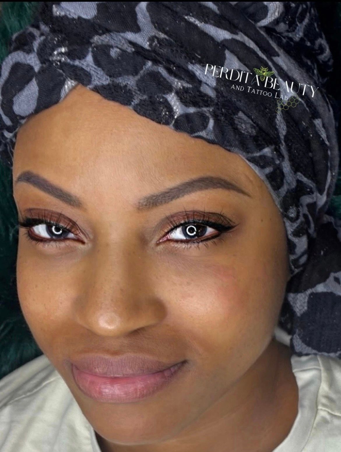 Close-up portrait of a woman with a patterned headwrap, soft makeup, and a slight smile.