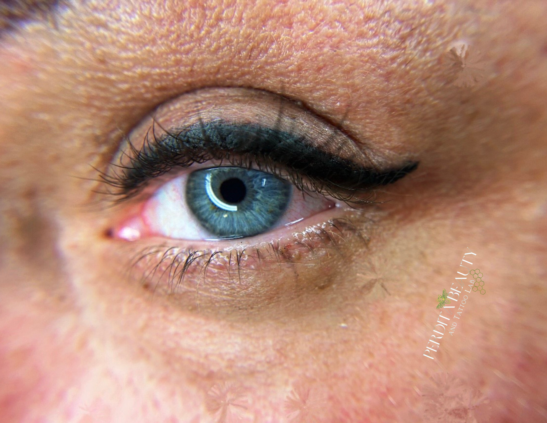 Close-up of a blue eye with black eyeliner and mascara on a light skin face.
