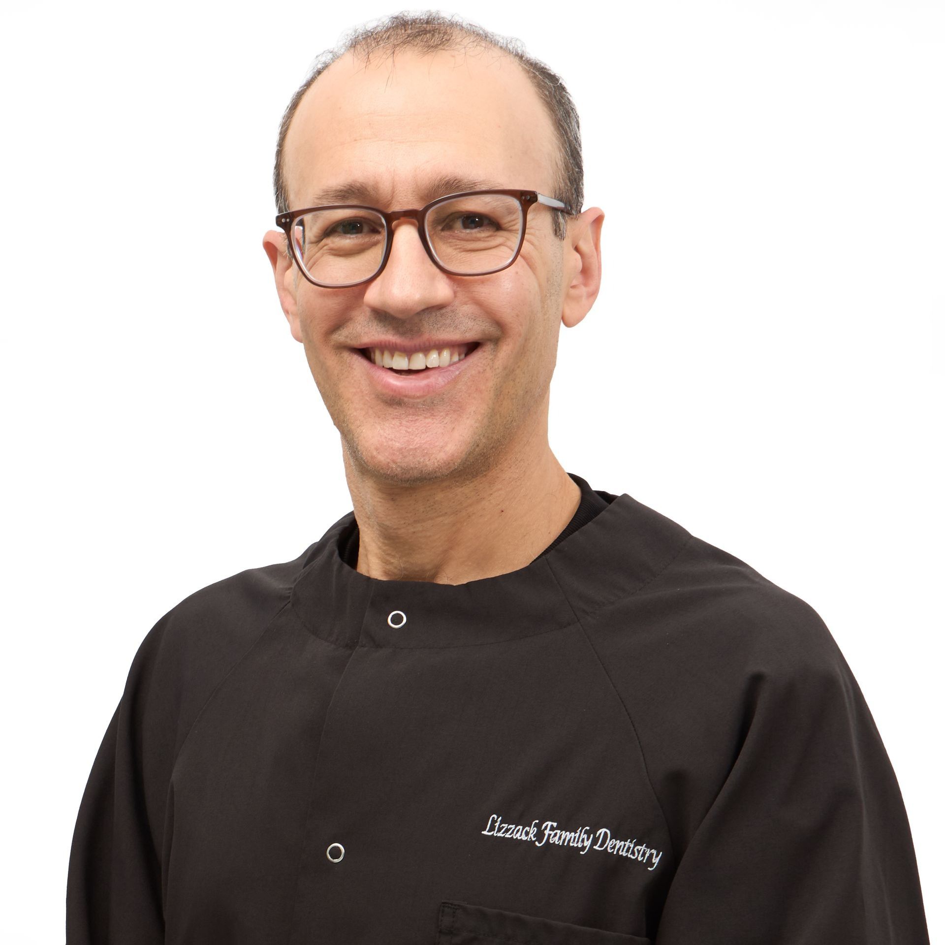 A smiling man wearing glasses and a black dental coat with