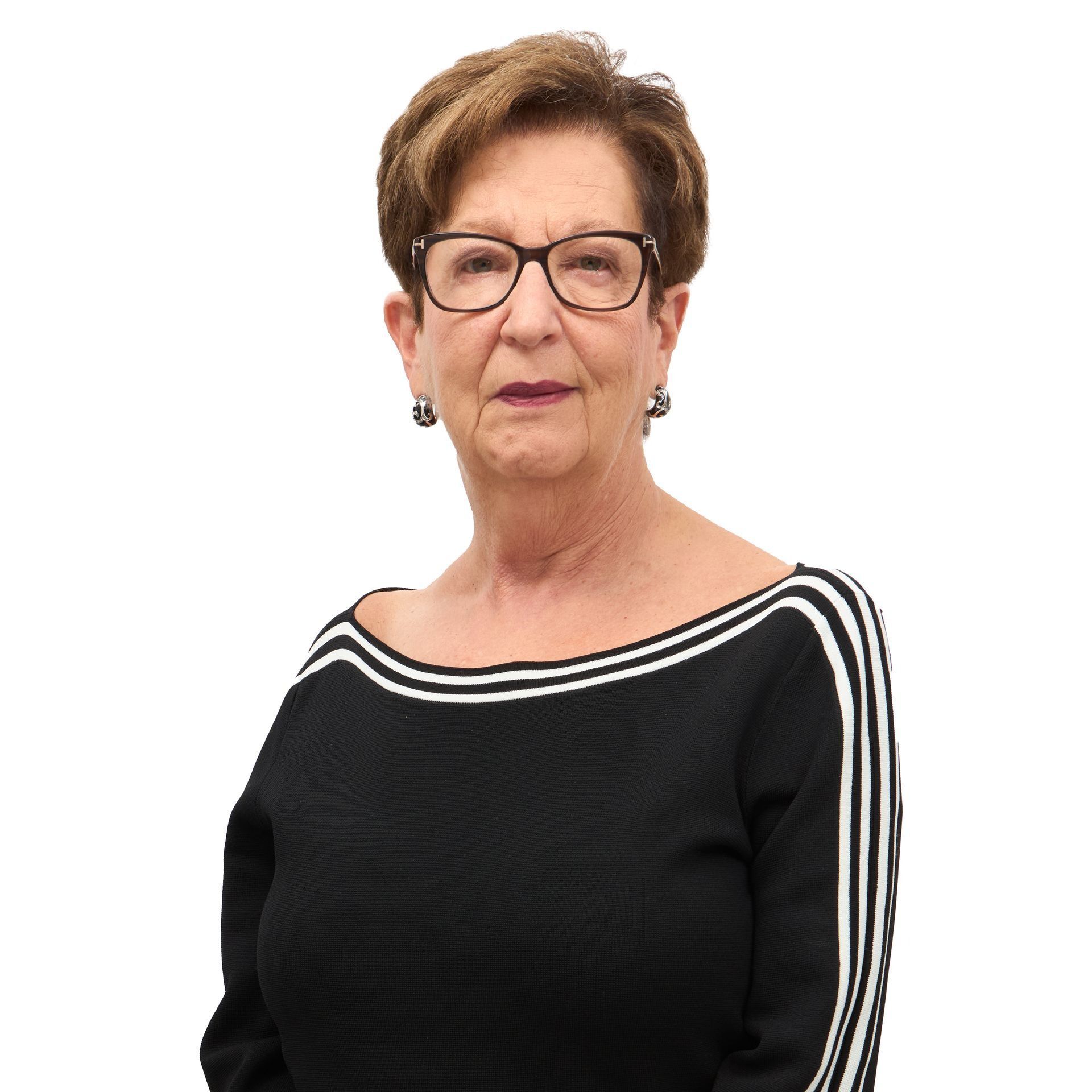 An older woman with short brown hair and glasses, wearing a black top with white stripes. She is smiling slightly.