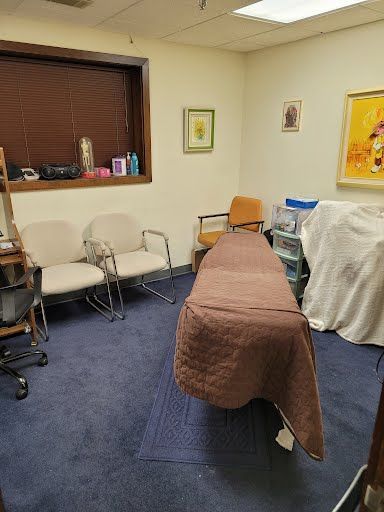 Room with massage table, chairs, artwork, and blue carpet.