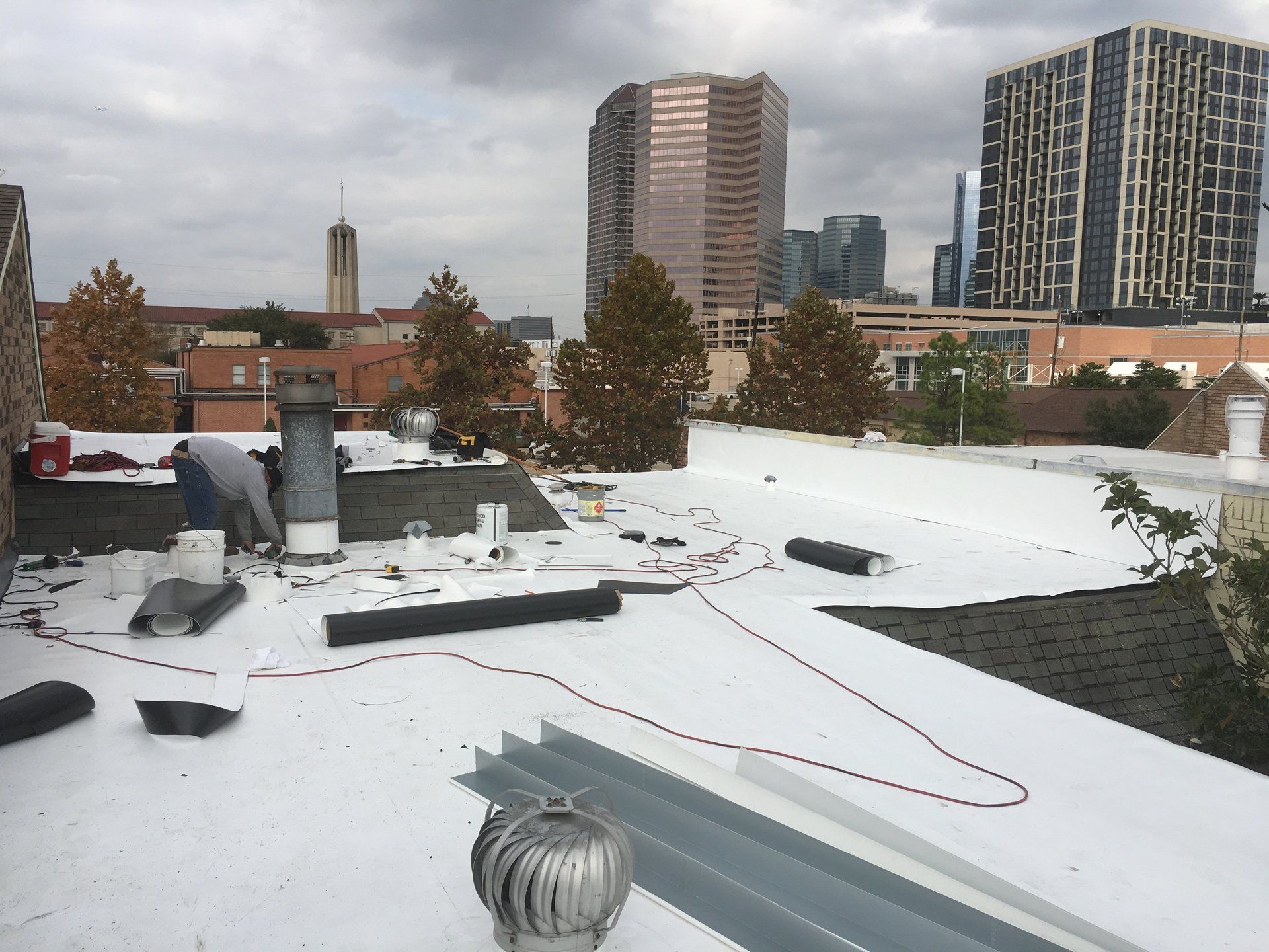 A man is working on a white roof with a city in the background