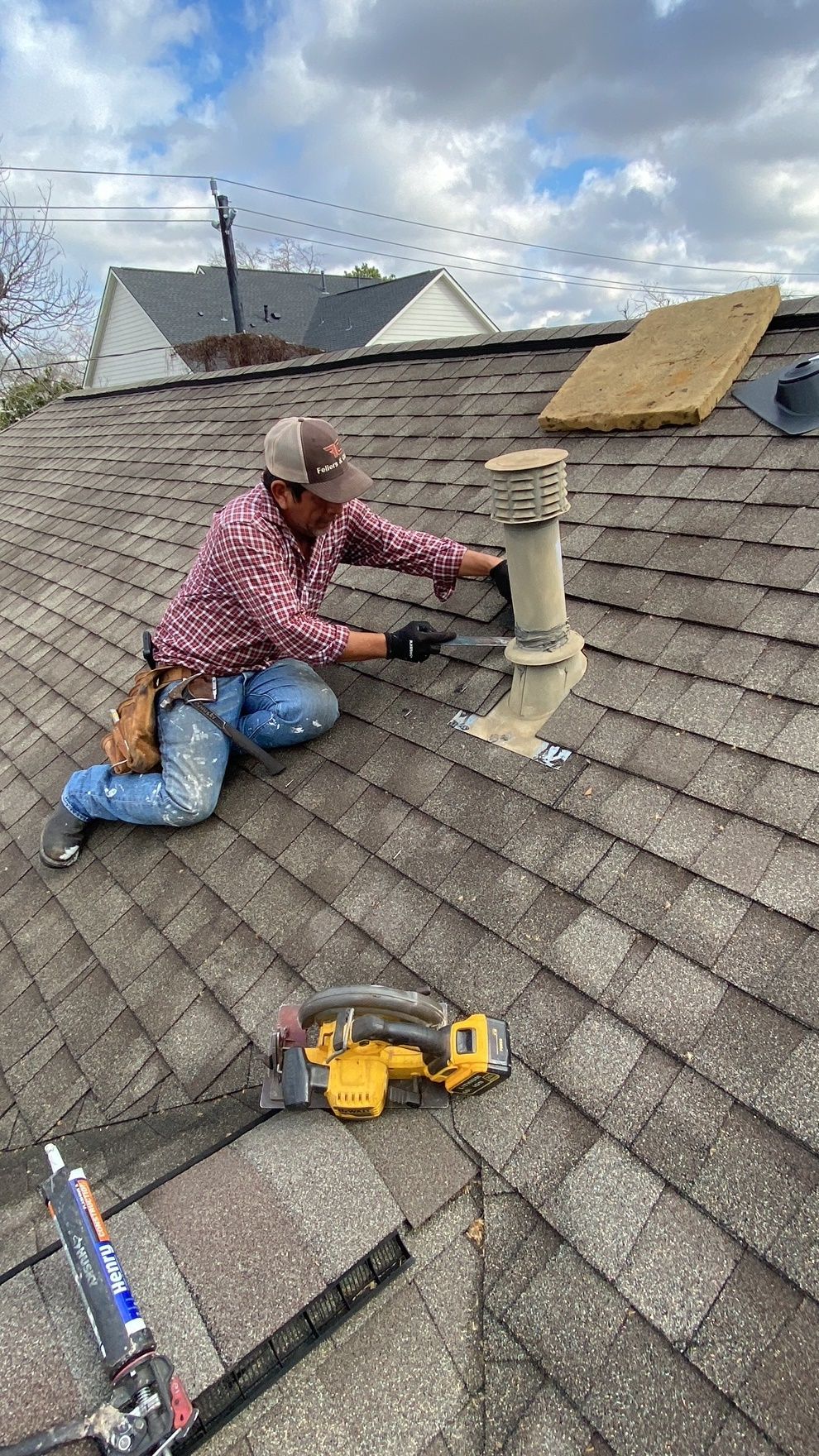 A man is kneeling on a roof working on a chimney.