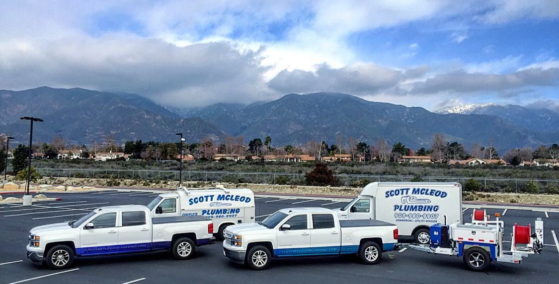 Three white service trucks parked; backdrop of mountains. The trucks have blue trim and company logo.