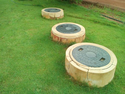 Three round concrete covers set in a grassy lawn, with the nearest one in the foreground.